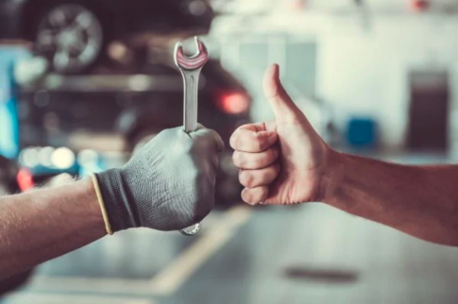 A hand with a work glove giving a thumbs up and a hand holding a wrench